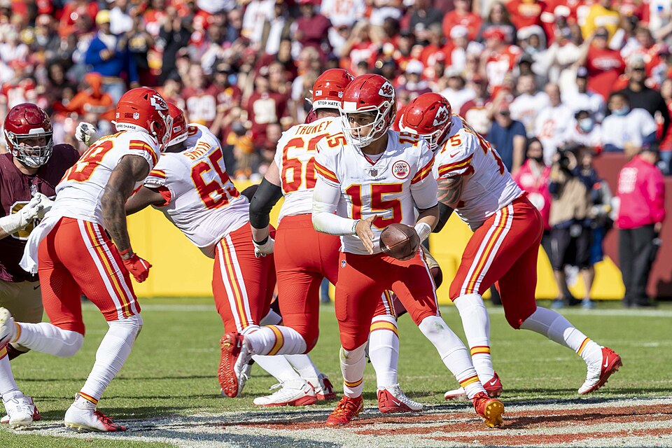 Patrick Mahomes carrying the football in his white Kansas City Chiefs #15 uniform during a 2021 game. Player photograph, not card artwork.