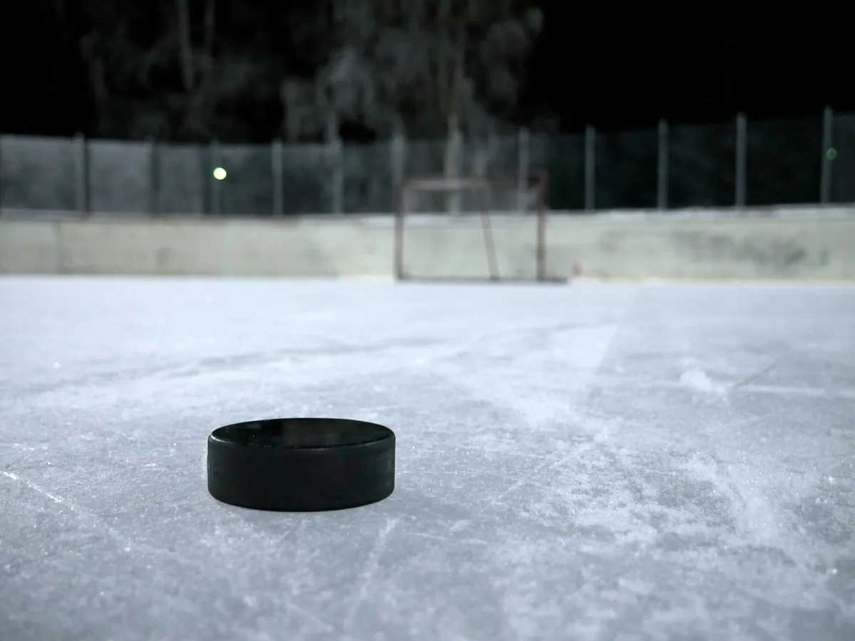 A black hockey puck on empty ice with a goal in the background.